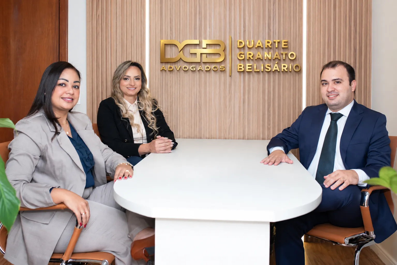 Os três sócios da DGB Advogados reunidos à mesa do escritório, com o logotipo ao fundo